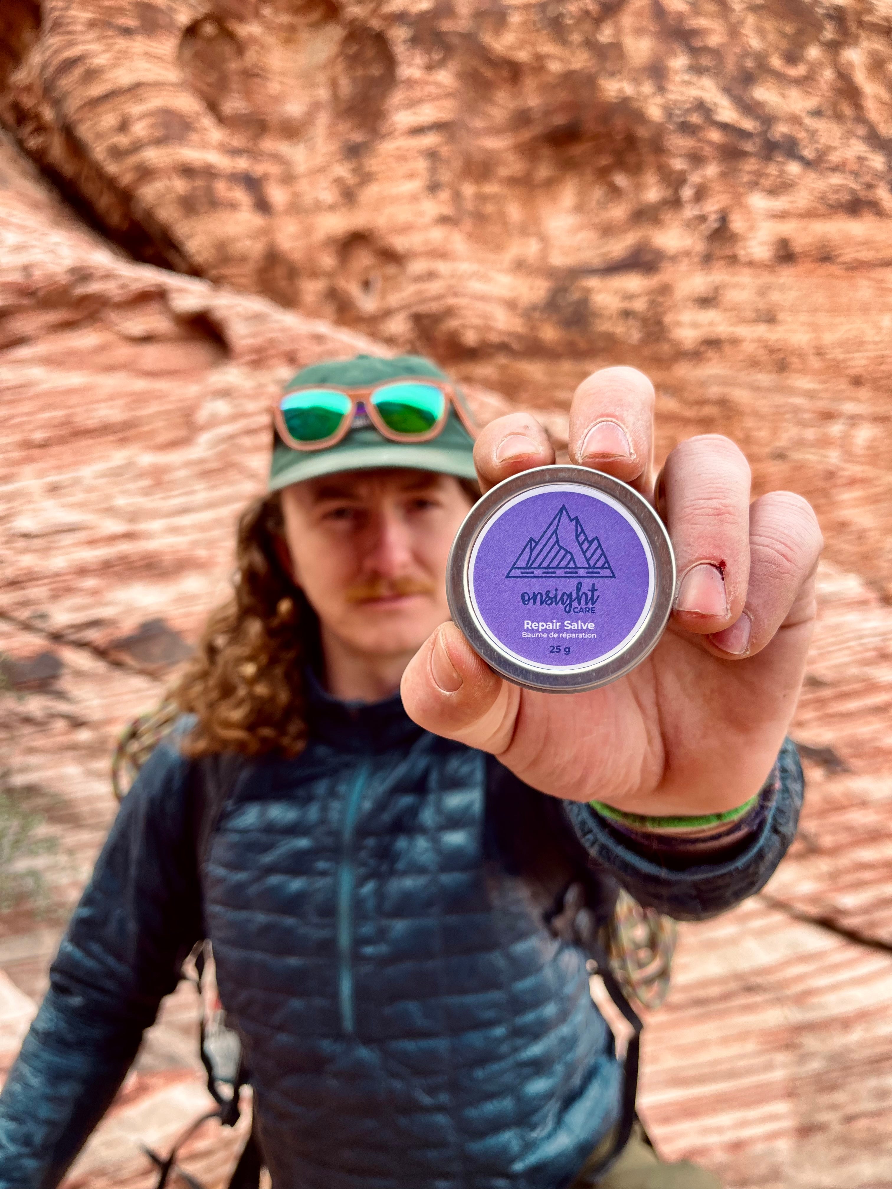 Man holding repair balm in front of red rocks climbing area. 