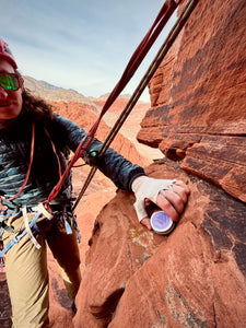 Rock climber reaching for skin repair salve while hanging on mountain face in Red Rocks Canyon.