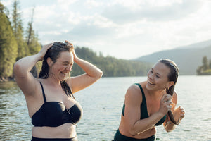 two females washing hair with shampoo bars, in lake with mountain and forest bachground
