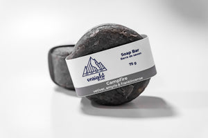 round charcoal soap bar leaning on label front of other bar.
