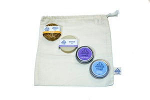 Cotton bulk bag with shampoo bar, deodorant bar, skin salve, and tooth powder laying on top in a diagonal.