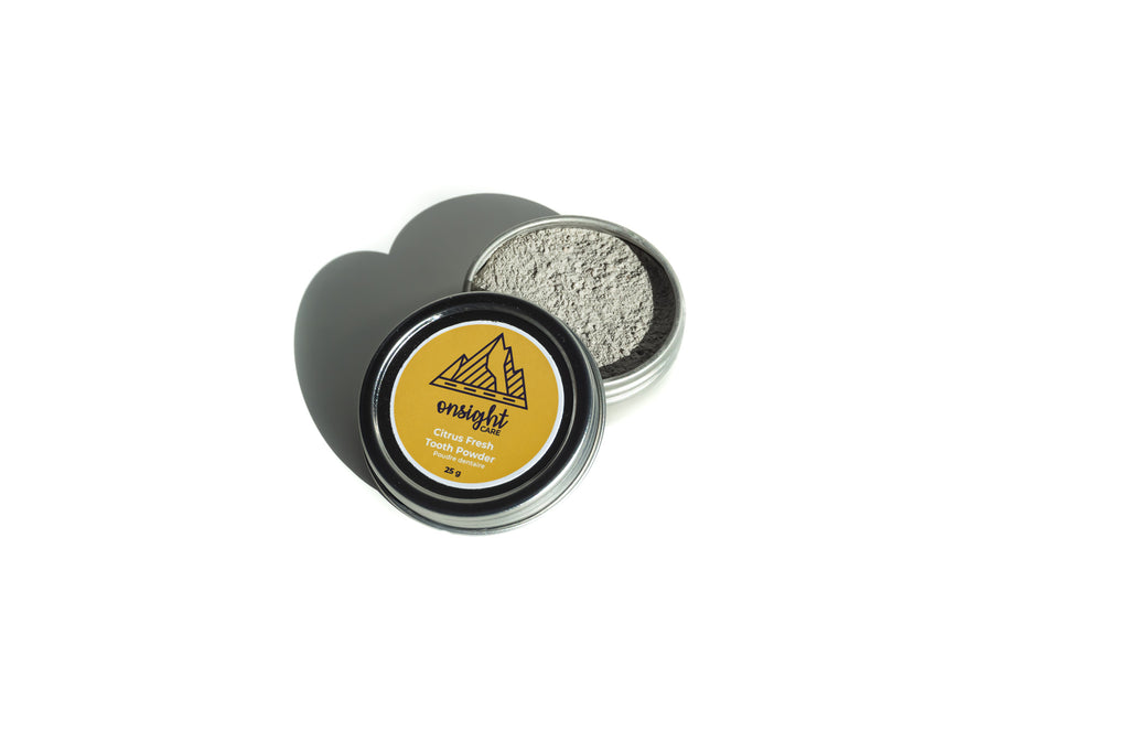 opened tin with grey tooth powder showing and yellow labeled lid leaning on top.