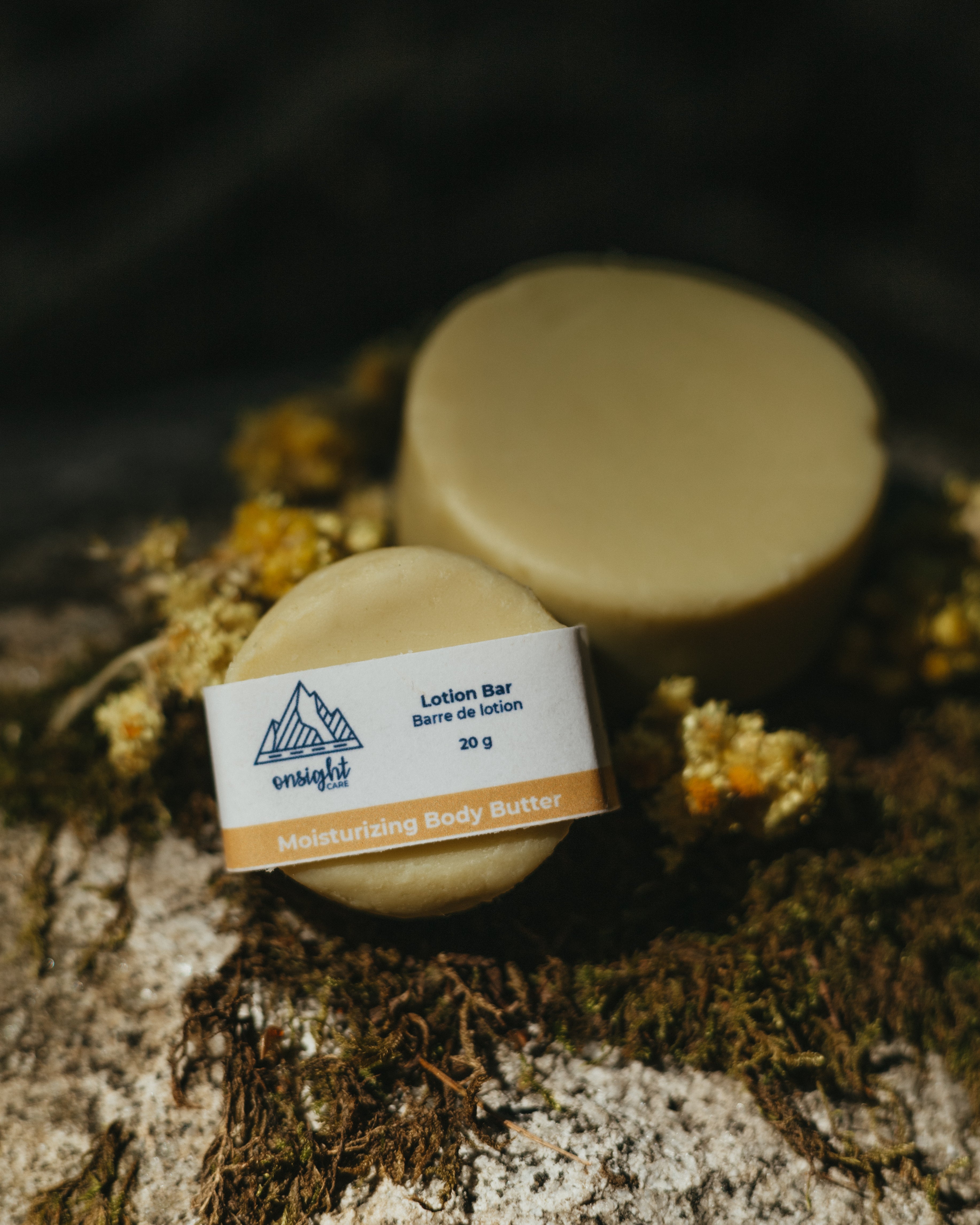 clean, natural lotion bar placed on mossy rock with helichrysum flowers sprinkled around.
