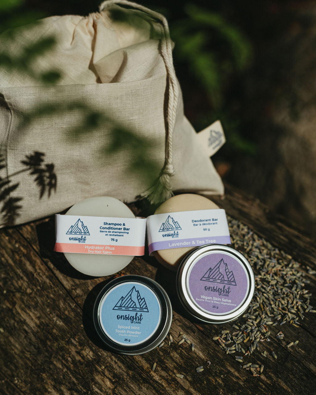 white cotton bulk bag sitting on log with shampoo & conditioner bar, deodorant bar, tooth powder, and skin salve leaning against. Leaves and lavender spilling over products.
