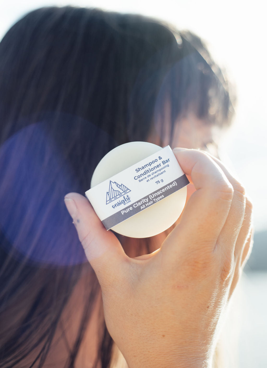 Travel Pure Clarity shampoo bar held up in front of dark hair and sunlight behind.